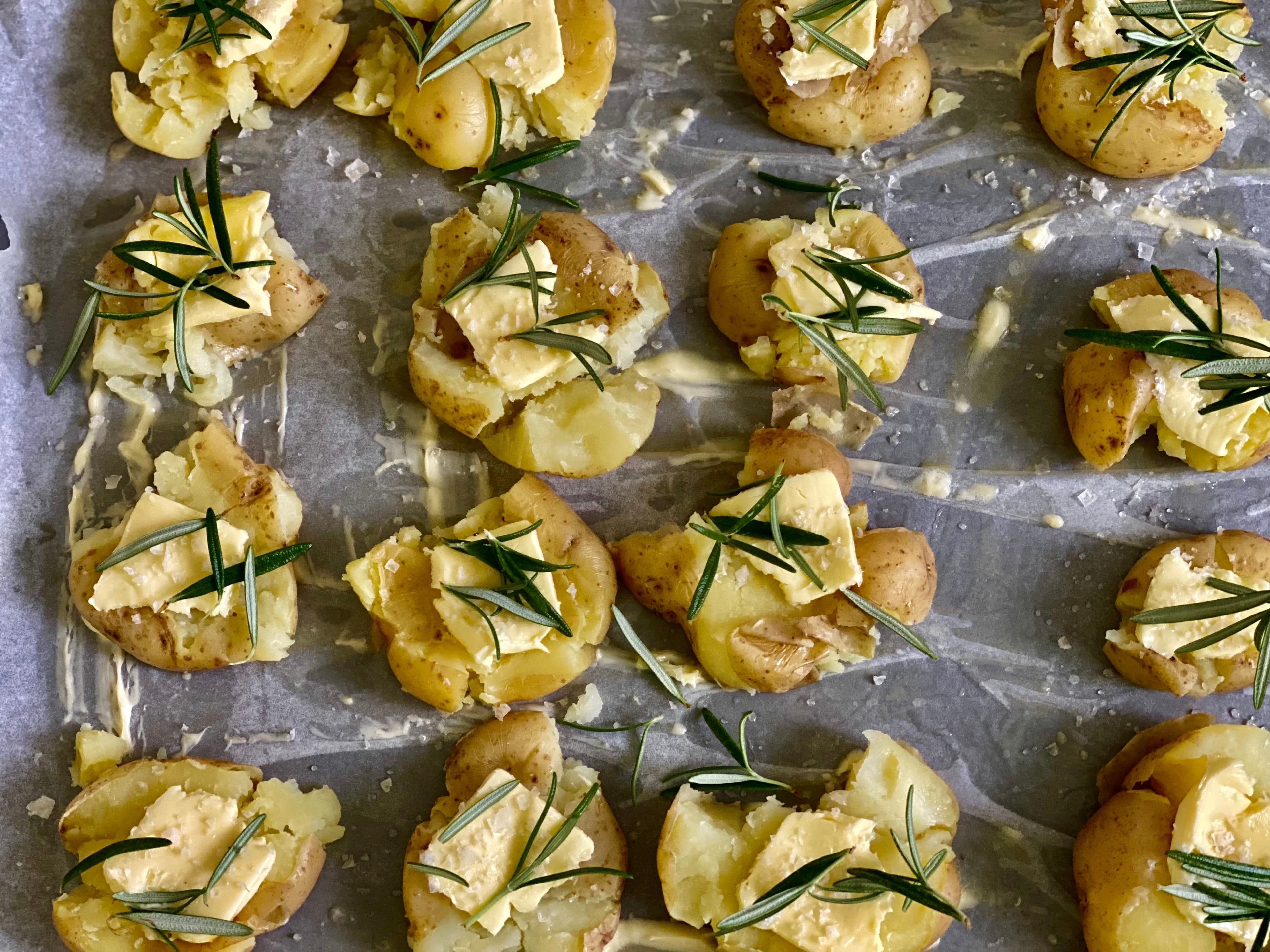 a tray with squashed potatoes, butter and rosemary