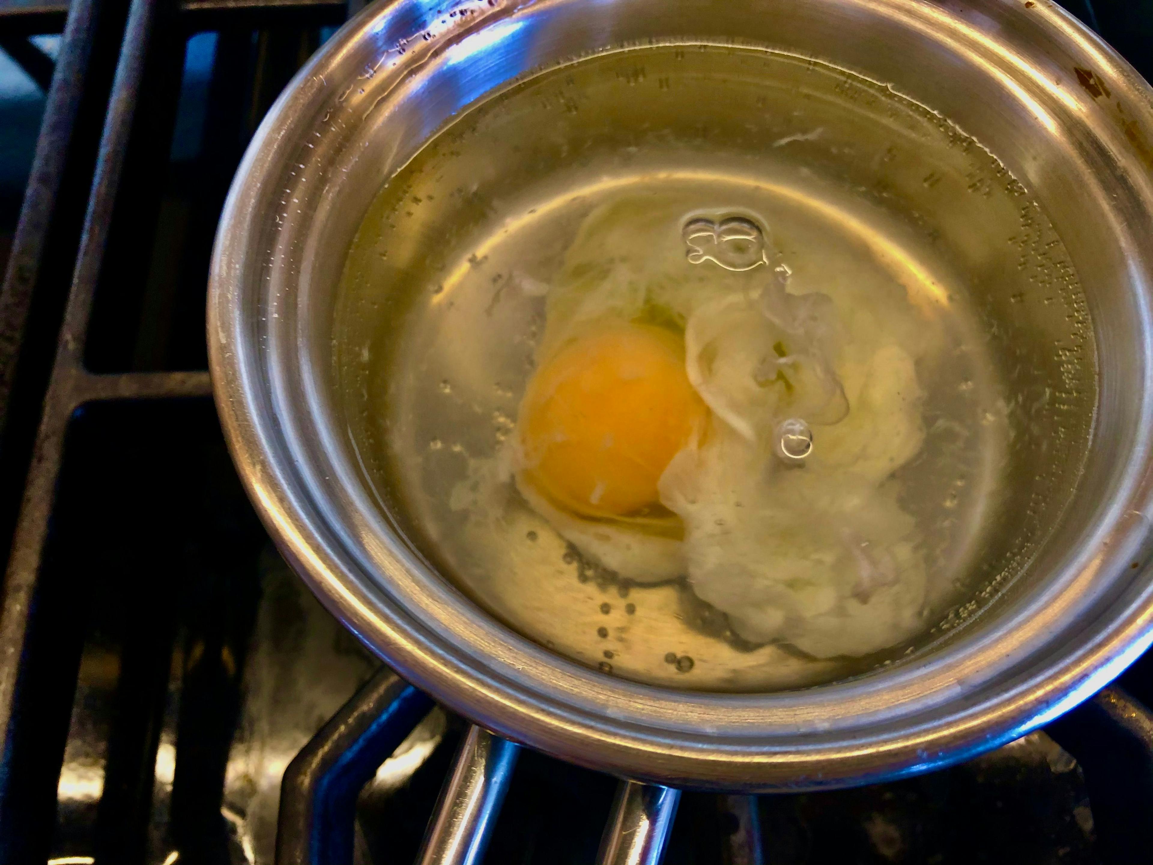 sauce pan with water and egg being poached