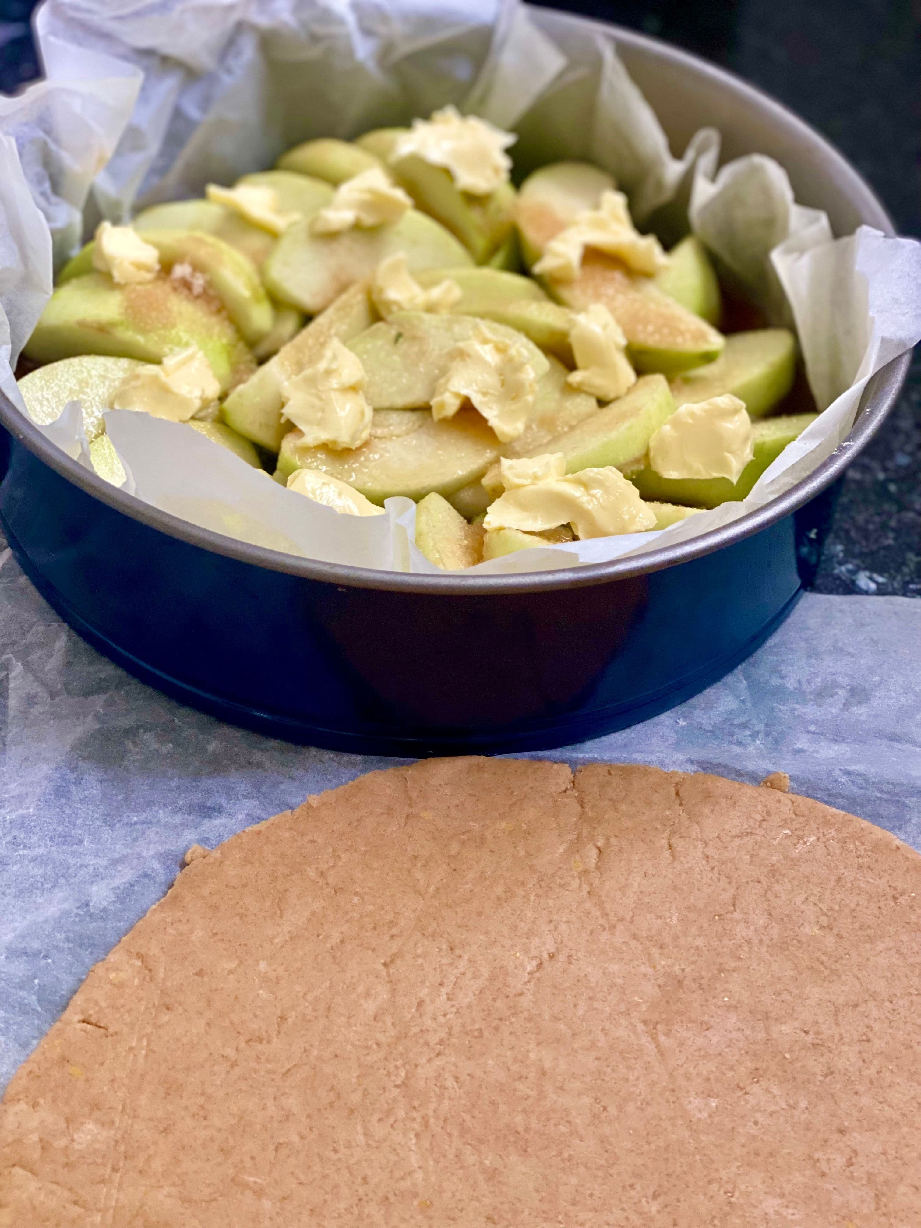 pie dish with apples and butter and rolled out pastry