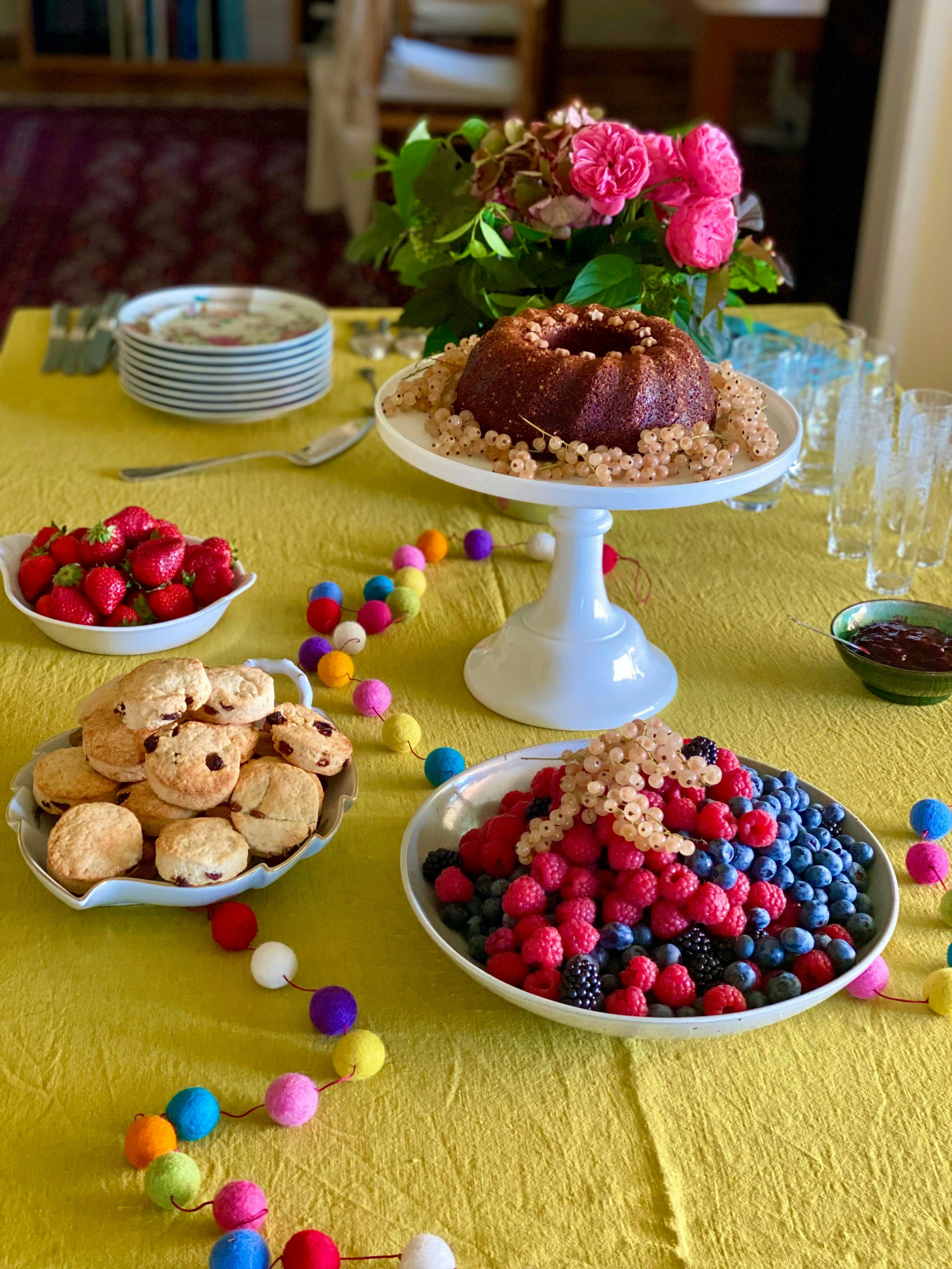 table with decorated cake, berries, strawberries, scones and flowers