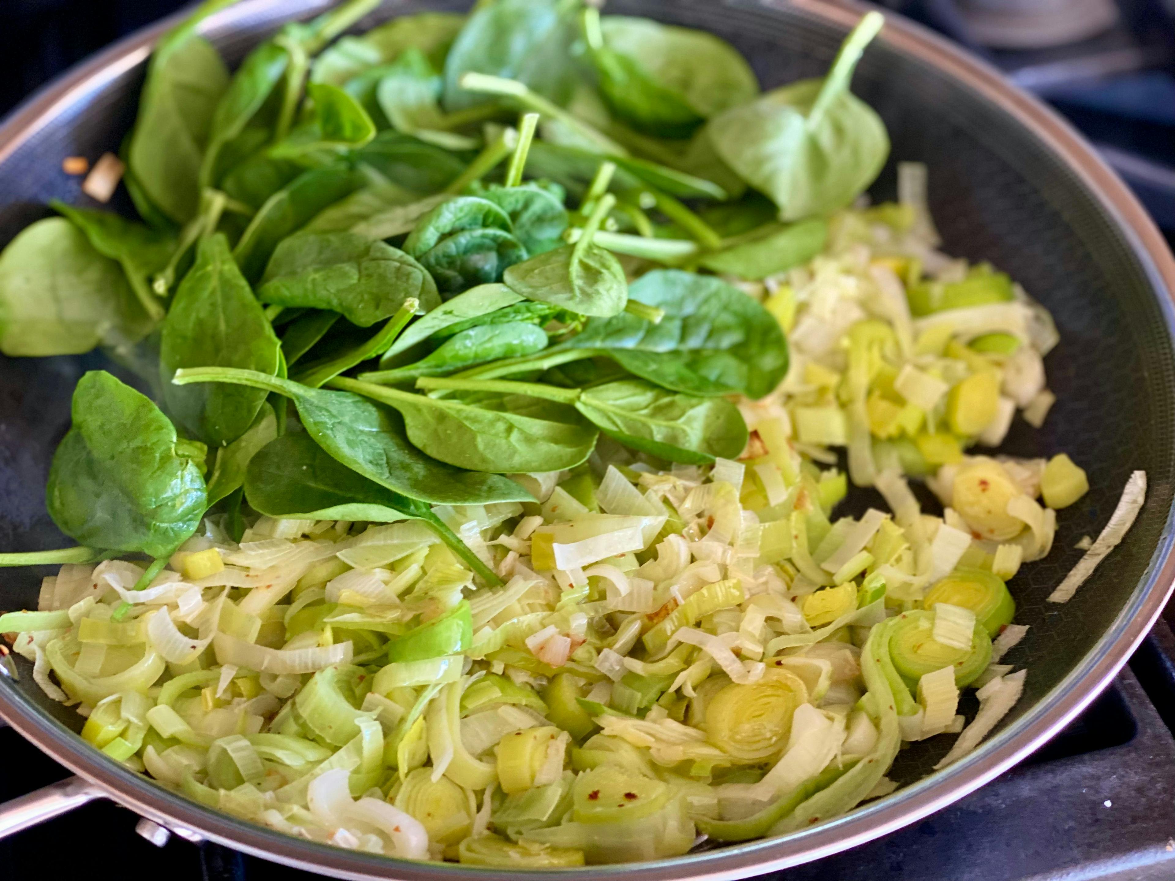 cooked leeks and fresh spinach in a fry pan